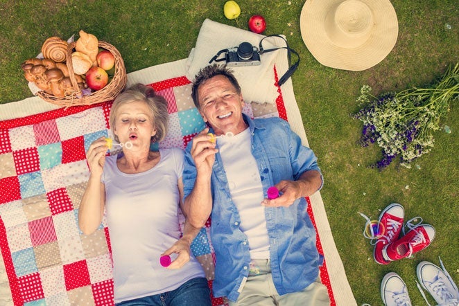 A couple enjoying the benefits of aging while picnicking with bubbles|A woman enjoying the benefits of aging on the beach|People on a run enjoying the benefits of aging|Two men enjoying the benefits of aging and learning how to knit