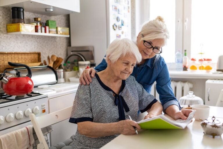 An elderly woman and her middle aged daughter look at documents to place her home in a trust